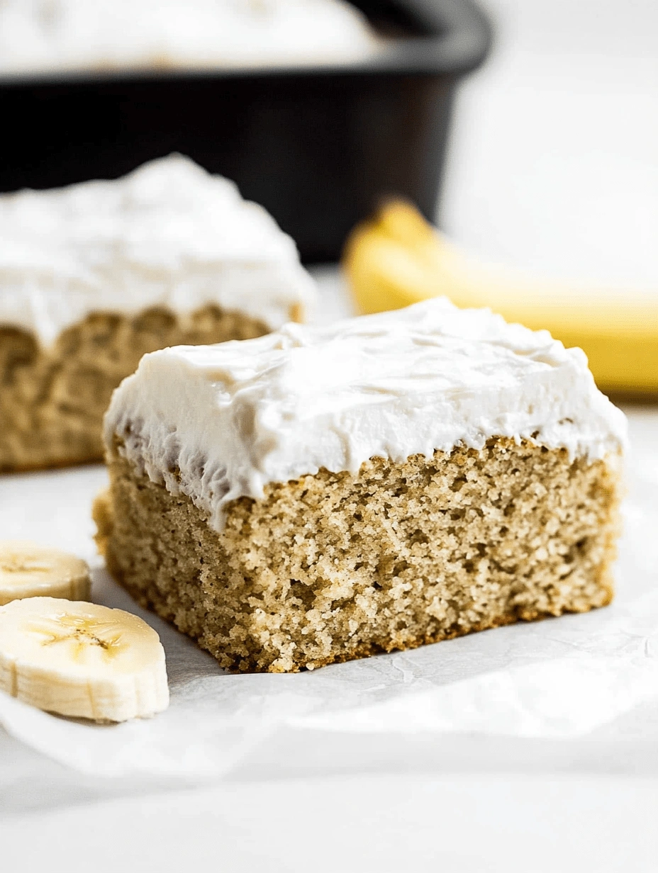 Square slice of healthy banana cake with whipped frosting and banana slices on white parchment