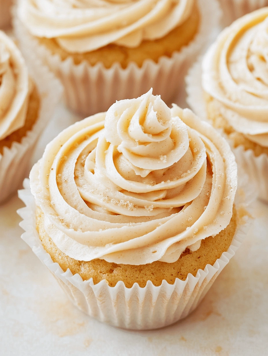 Close-up of a gluten-free cupcake with piped cinnamon-sugar frosting and a dusting of sugar, in a white paper liner.