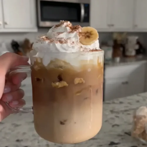 Homemade Dutch Bros Banana Bread Latte with whipped cream and banana slice held in a glass mug
